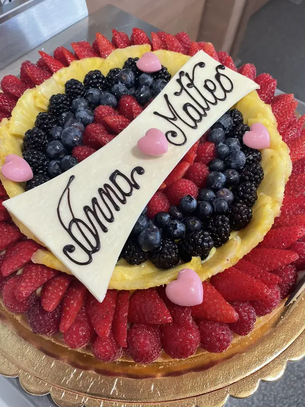 Torta di compleanno con frutta fresca e placca di cioccolato bianco personalizzata con i nomi